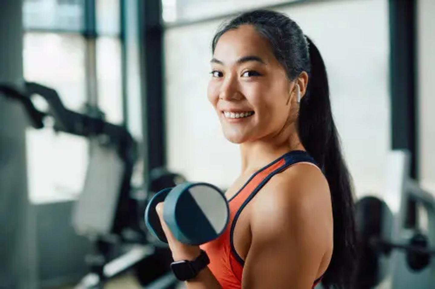 Asian female smiling to the camera, caring a weight while wearing AirPods