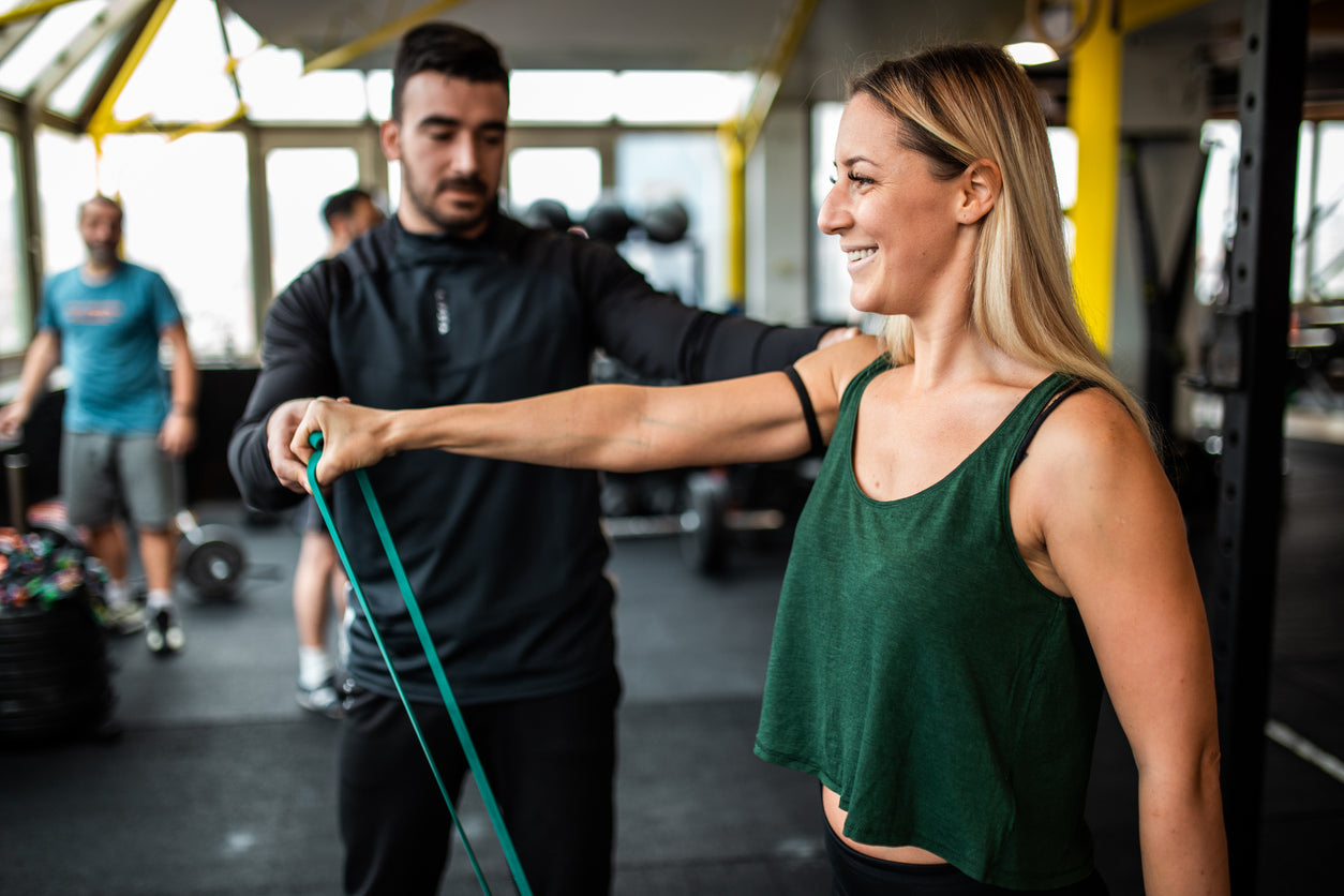 Trainer guiding a client through a shoulder resistance band exercise
