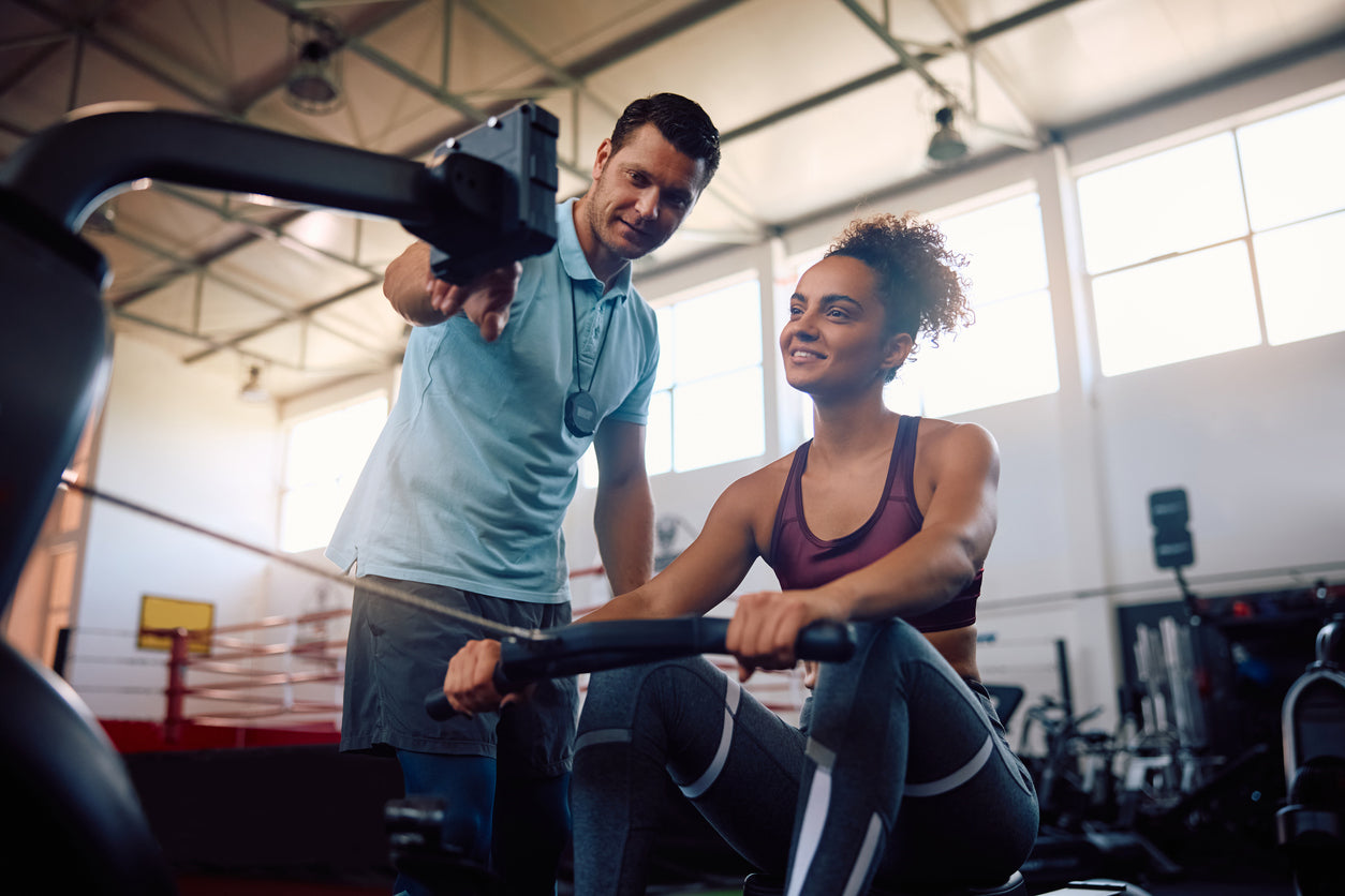 Trainer instructing a client on a rowing machine, stopwatch in hand