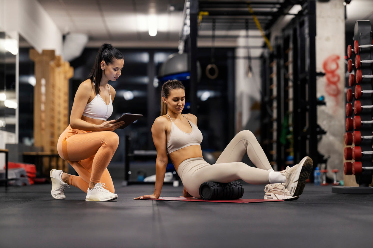 Coach monitoring a client's foam rolling technique with a tablet in hand