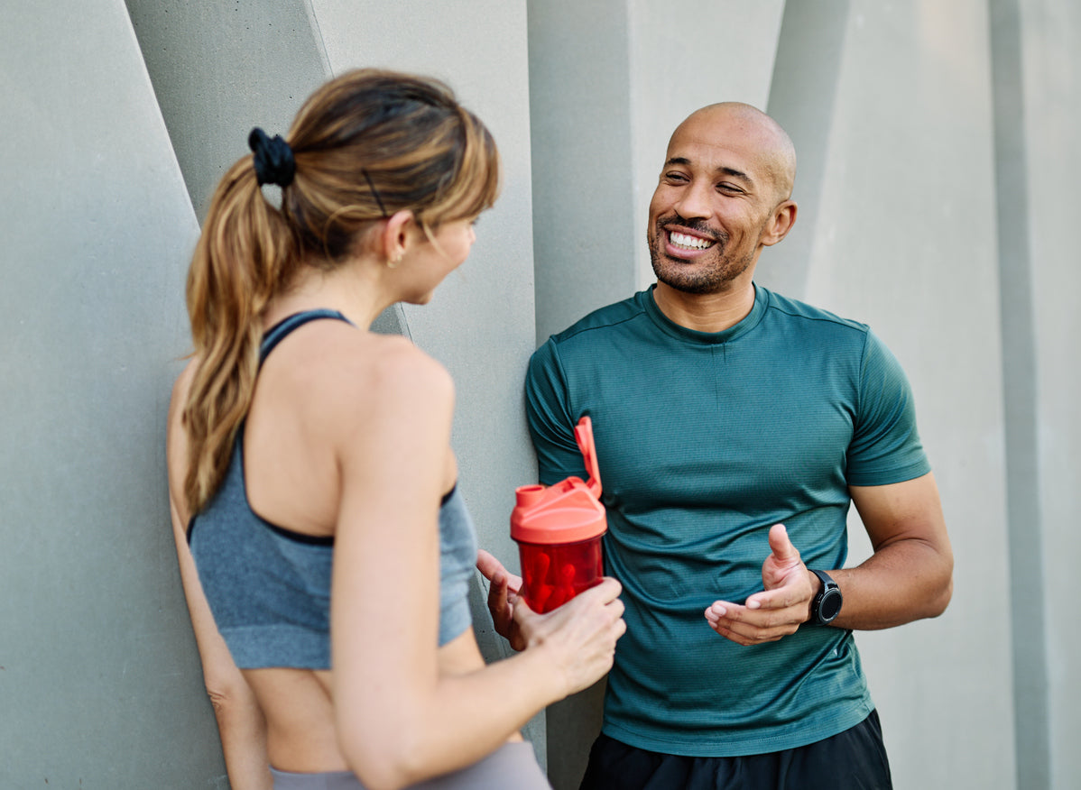 Trainer discussing hydration and nutrition strategy with a client holding a protein shaker